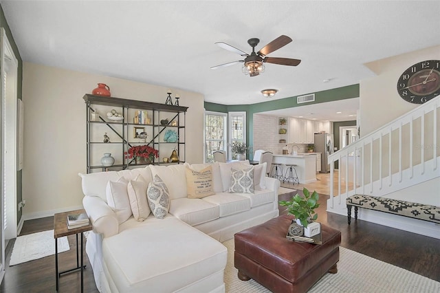 living area featuring baseboards, visible vents, a ceiling fan, stairway, and wood finished floors