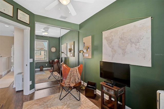 living area featuring baseboards, visible vents, a ceiling fan, and wood finished floors