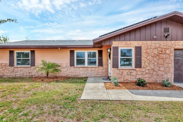 single story home with stone siding, a front lawn, and stucco siding