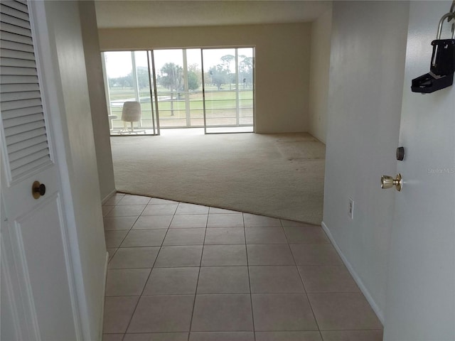 empty room with light colored carpet, baseboards, and light tile patterned floors