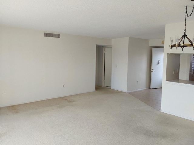 spare room featuring light carpet, light tile patterned floors, visible vents, and a textured ceiling