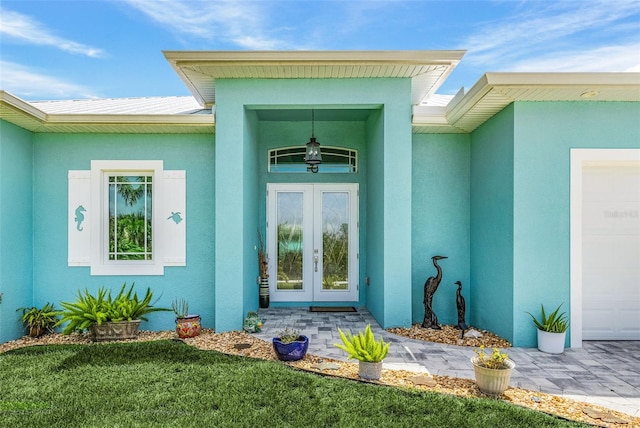 property entrance featuring a garage, a yard, french doors, and stucco siding