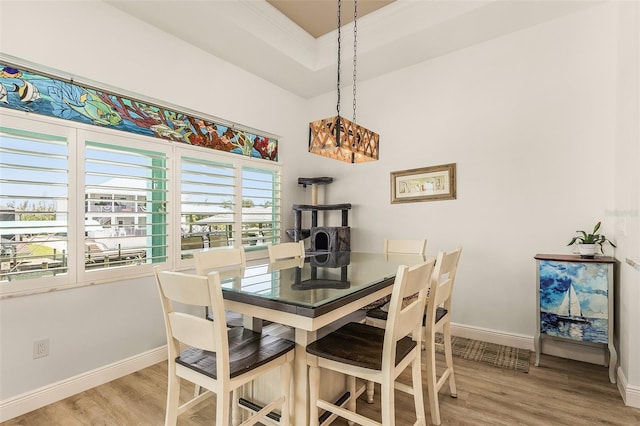 dining space with a tray ceiling, light wood finished floors, and baseboards