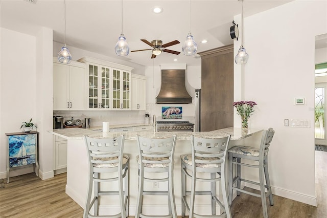 kitchen featuring white cabinetry, custom range hood, glass insert cabinets, and a kitchen breakfast bar