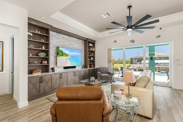 living area featuring visible vents, light wood-style floors, built in features, ornamental molding, and a raised ceiling