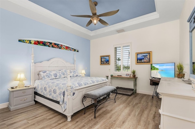 bedroom featuring light wood-style flooring, visible vents, a tray ceiling, and baseboards