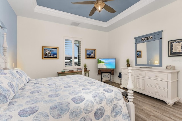 bedroom with ceiling fan, visible vents, light wood-style floors, a raised ceiling, and crown molding