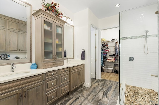 full bathroom with double vanity, a stall shower, a walk in closet, and a sink