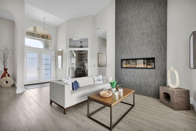 living area with french doors, a fireplace, visible vents, wood finished floors, and high vaulted ceiling