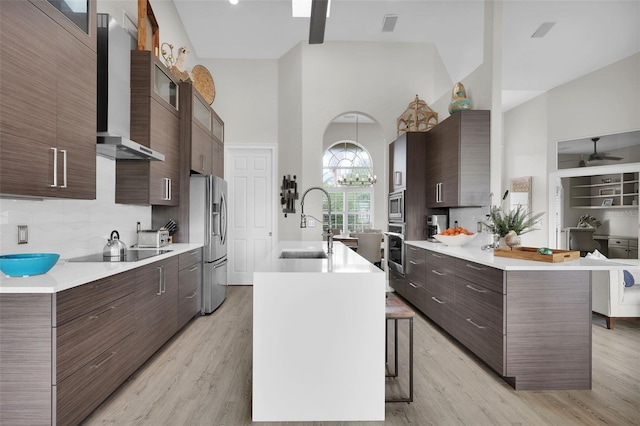 kitchen with light countertops, appliances with stainless steel finishes, a sink, wall chimney range hood, and a kitchen breakfast bar