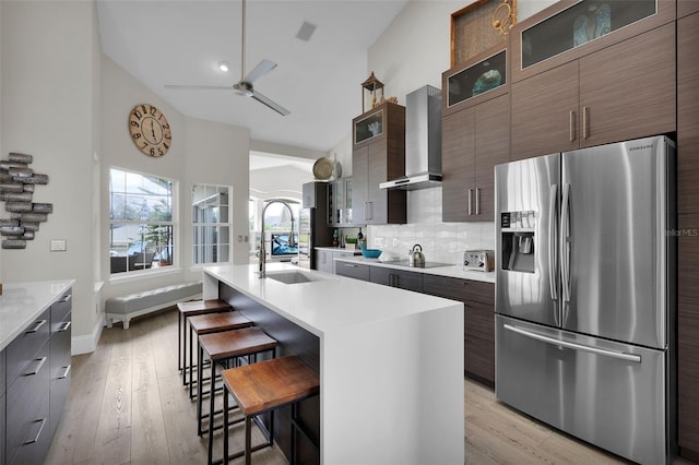 kitchen with wall chimney range hood, modern cabinets, stainless steel fridge, and a breakfast bar