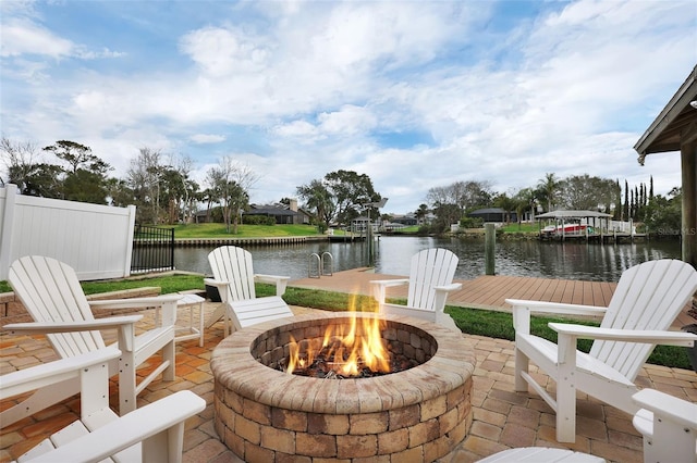 view of patio with a dock, a water view, fence, and a fire pit