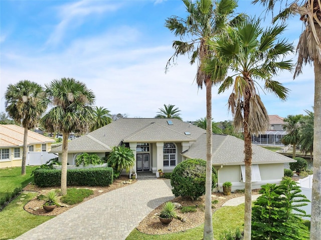 view of front of property featuring fence, french doors, roof with shingles, decorative driveway, and stucco siding