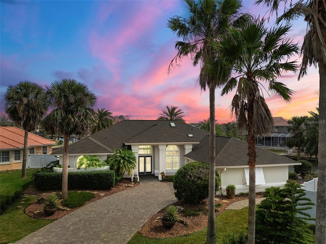 view of front of property featuring decorative driveway, french doors, fence, and stucco siding