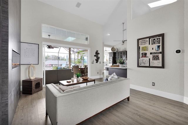 living room with ceiling fan, wood finished floors, a towering ceiling, and baseboards