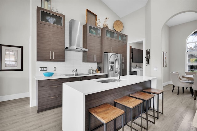 kitchen featuring black electric cooktop, a kitchen breakfast bar, wall chimney range hood, stainless steel refrigerator with ice dispenser, and washer and clothes dryer