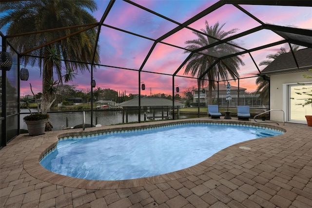 pool at dusk with a water view, glass enclosure, an outdoor pool, and a patio