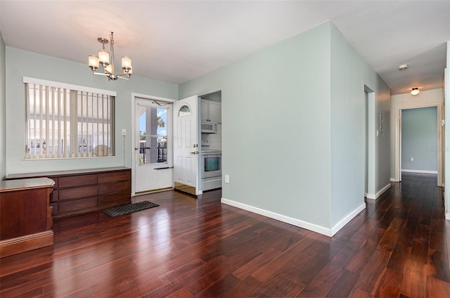 entryway with an inviting chandelier, dark wood finished floors, and baseboards