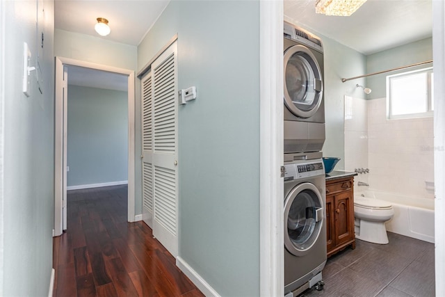 laundry area featuring dark wood-style floors, stacked washer / drying machine, laundry area, and baseboards