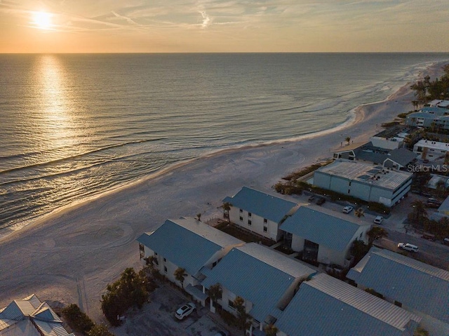 aerial view at dusk featuring a water view and a beach view