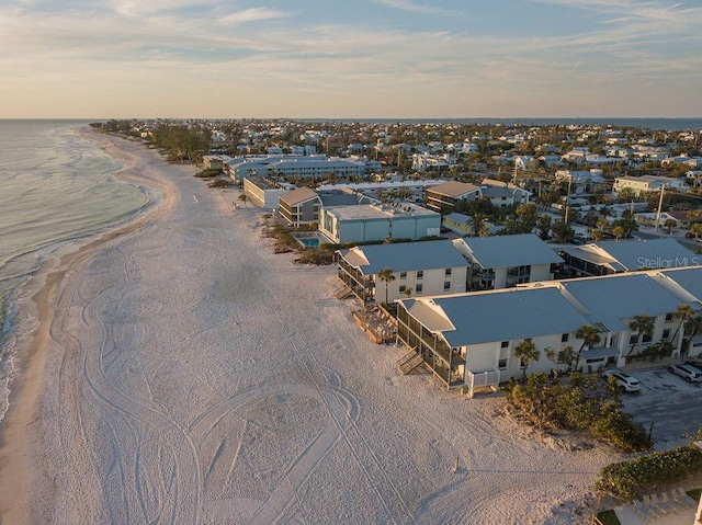 aerial view at dusk featuring a water view and a beach view