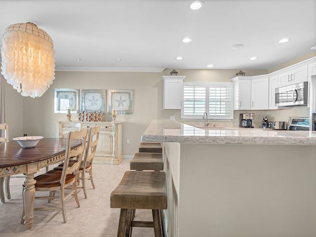 kitchen featuring light stone counters, a breakfast bar area, recessed lighting, white cabinets, and stainless steel microwave