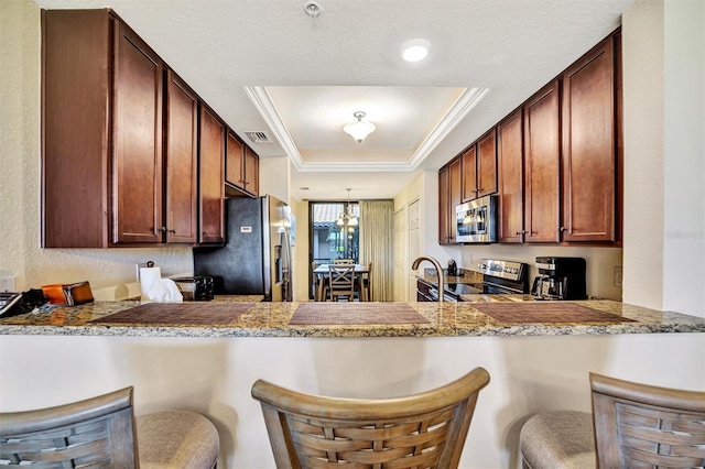 kitchen featuring stainless steel appliances, a breakfast bar, a peninsula, and a raised ceiling