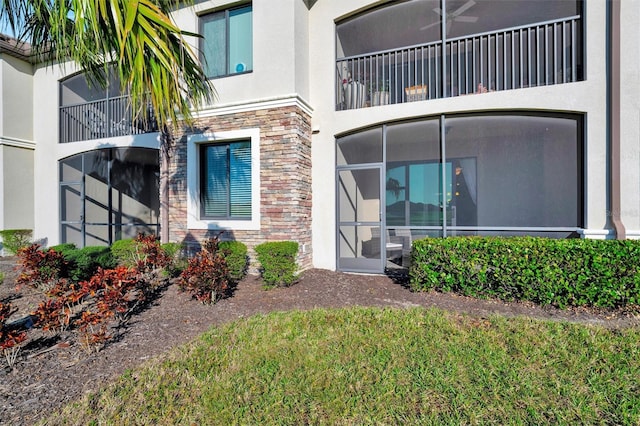 doorway to property with stone siding, a lawn, and stucco siding