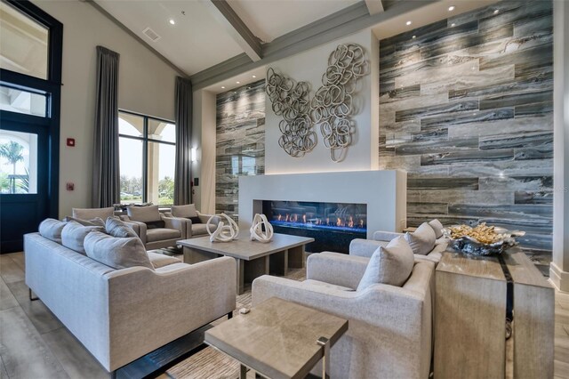 living area with high vaulted ceiling, visible vents, a healthy amount of sunlight, beamed ceiling, and a glass covered fireplace