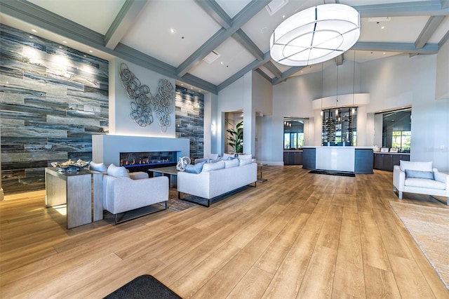 living room featuring an accent wall, a healthy amount of sunlight, beam ceiling, light wood finished floors, and a glass covered fireplace