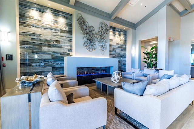 living area featuring beam ceiling, a high ceiling, an accent wall, a glass covered fireplace, and wood finished floors