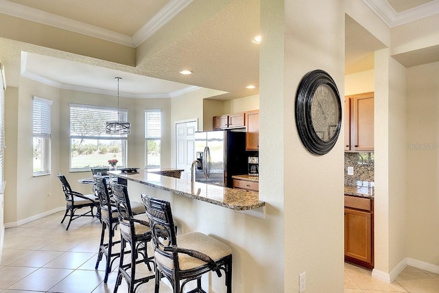 kitchen featuring decorative backsplash, stainless steel fridge, crown molding, and a breakfast bar area