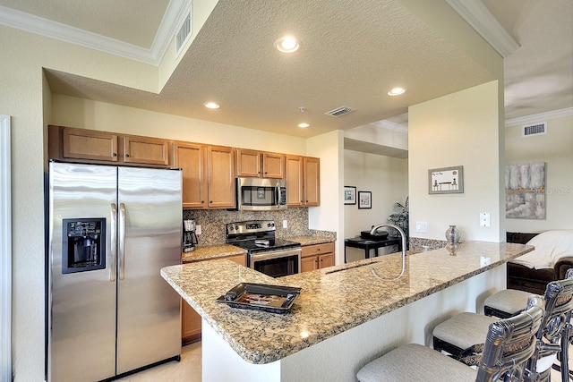 kitchen featuring visible vents, a peninsula, stainless steel appliances, crown molding, and a sink