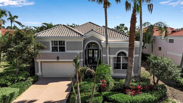 mediterranean / spanish home featuring a garage, a tiled roof, decorative driveway, and stucco siding