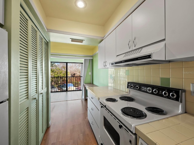 kitchen with under cabinet range hood, white electric range, light wood-style floors, white cabinets, and decorative backsplash