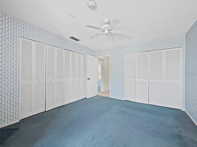 unfurnished bedroom featuring a textured ceiling, visible vents, multiple closets, dark colored carpet, and wallpapered walls