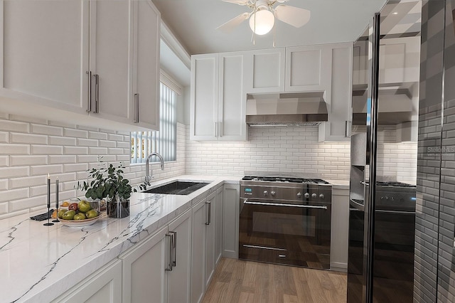 kitchen with light stone countertops, wall chimney exhaust hood, high end range, and a sink
