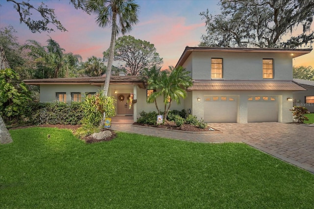 view of front of property with an attached garage, a yard, decorative driveway, and stucco siding