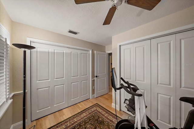 exercise room featuring a textured ceiling, light wood-style flooring, visible vents, and a ceiling fan