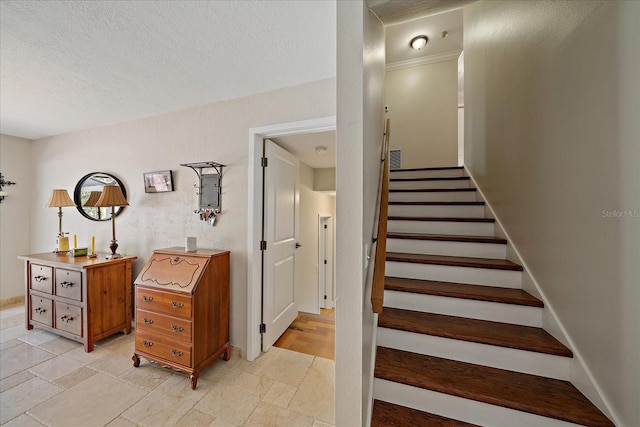 stairway featuring stone finish floor, visible vents, a textured ceiling, and baseboards