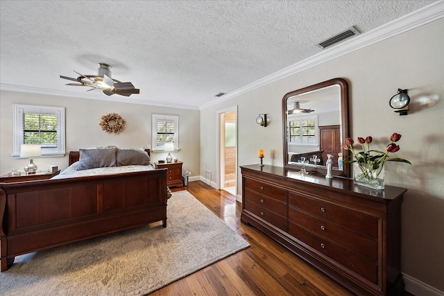 bedroom featuring baseboards, visible vents, ornamental molding, wood finished floors, and a textured ceiling