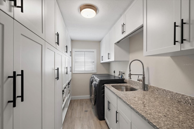 clothes washing area featuring cabinet space, baseboards, washing machine and clothes dryer, light wood-style floors, and a sink