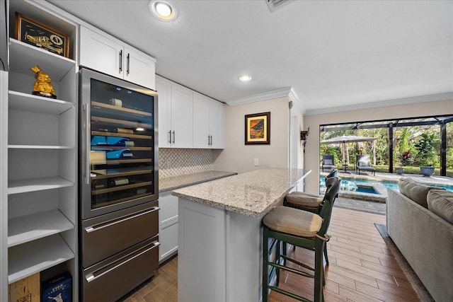 kitchen featuring crown molding, backsplash, open floor plan, white cabinetry, and light stone countertops