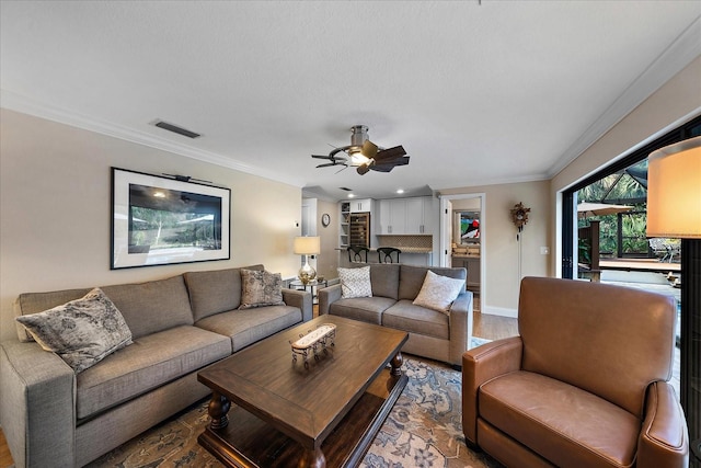 living room featuring ceiling fan, wood finished floors, visible vents, baseboards, and crown molding