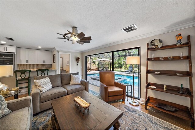 living area featuring a textured ceiling, wood finished floors, visible vents, and crown molding