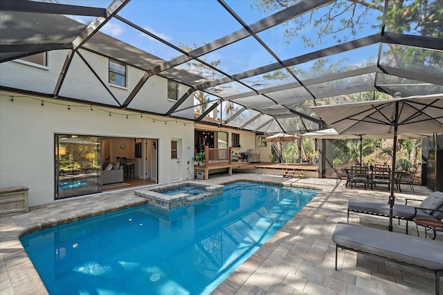 view of swimming pool featuring a patio area, a pool with connected hot tub, glass enclosure, and a wooden deck