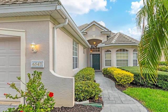 view of exterior entry featuring a garage, a tile roof, and stucco siding