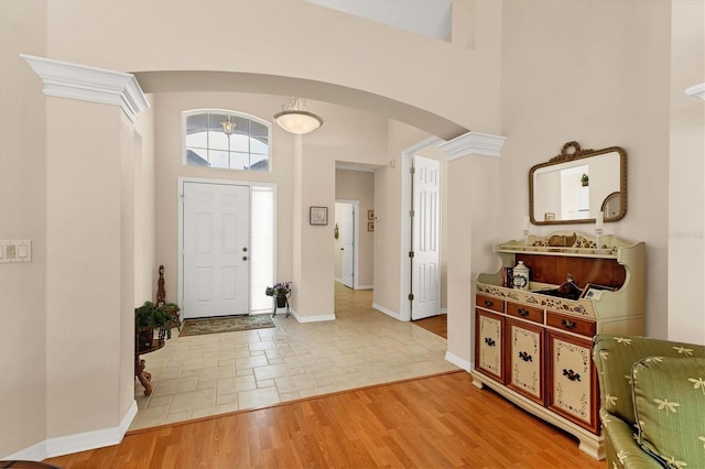 entrance foyer with arched walkways, a high ceiling, light wood-style flooring, and baseboards