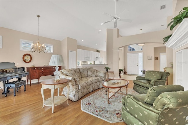 living room featuring visible vents, arched walkways, light wood-style floors, high vaulted ceiling, and ceiling fan with notable chandelier