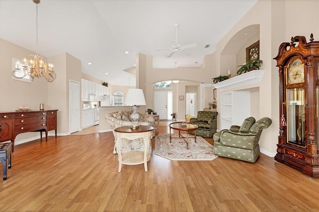 living area featuring light wood finished floors, baseboards, arched walkways, and ceiling fan with notable chandelier